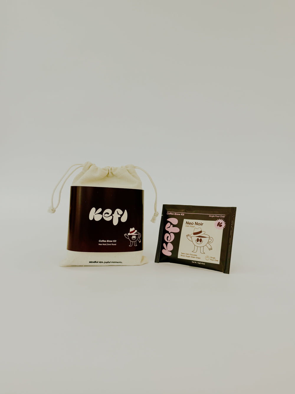 A cream-colored drawstring pouch and a small square packet with a cartoon character and the word 'Kopi' on a plain light gray background.